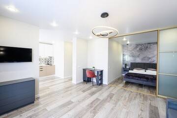 modern apartment interior featuring a living area, visible kitchen, and a bedroom mirrored by...