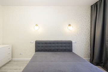serene bedroom featuring a gray bed with a tufted headboard, flanked by modern sconces. A white...