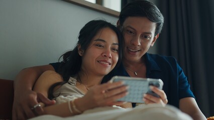 Young couple using smartphone together in bed, enjoying intimacy and connection
