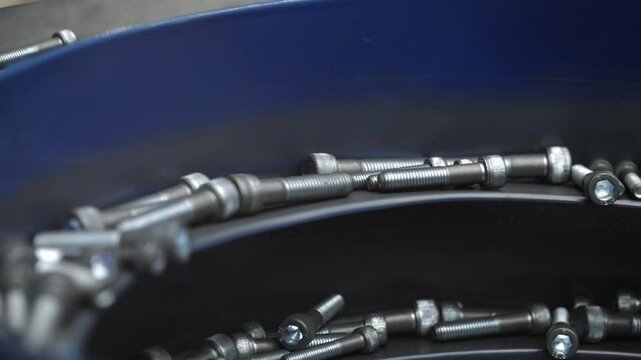 Close-up of metal bolts aligned and moving through a vibratory feeder system in an industrial production environment, illustrating precision engineering in action.