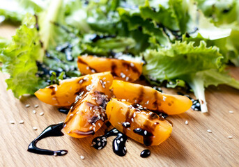 Sliced tomatoes drizzled with sauce and sprinkled with sesame seeds on a wooden cutting board. Close-up of tomatoes and lettuce. Concept of healthy eating and organic farm products.