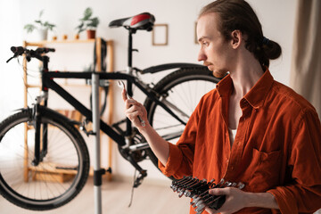 Young man choosing wrench for bicycle repair and maintenance at home