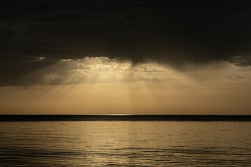 Dark storm clouds with golden sunlight breaking through over calm ocean water