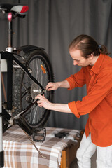 Young man with long hair repairing bicycle at home fixing wheel with special tool. Bicycle...