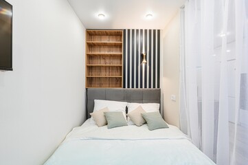  compact bedroom features a neatly made bed with white linens and pastel pillows. Above the bed is...