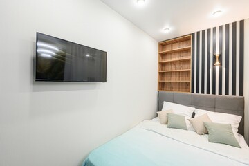 modern bedroom features a TV on a white wall, a grey bed, a bookcase, and black and white striped...