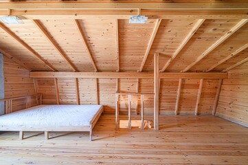 attic room with wooden walls, floor, and ceiling. A bed with a white mattress sits on the left, and...