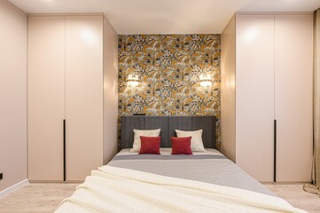 cozy bedroom featuring a bed with gray headboard, floral wallpaper, and built-in wardrobes,...