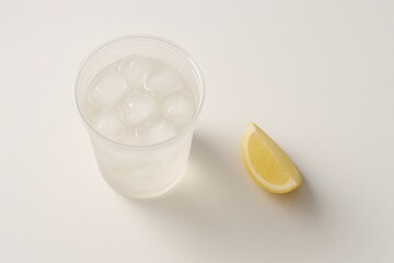 Clear plastic cup with ice cubes and lemon slice on white surface  