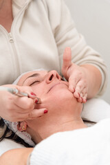 Beautician performing microdermabrasion treatment on mature woman face