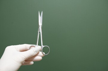 Gloved Hand Holding Surgical Scissors Against Green Background