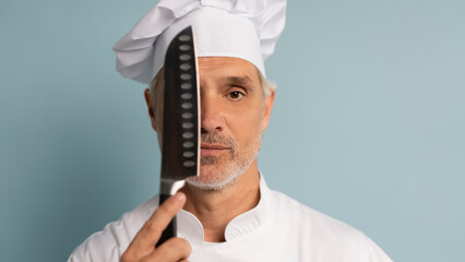 Portrait of a happy male chef cook holding knife isolated on a blue background
