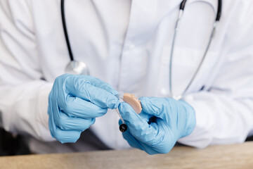 An otolaryngologist holds a hearing aid in his hands. The doctor consults the patient