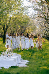 Women in white dresses stand in a field holding hands