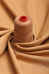 Summer fabric. Top down view of beige lightweight linen fabric with sewing thread resting atop. The...