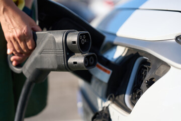 Mechanic plugging charging cable into electric car at station - sustainability and clean energy...