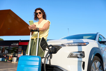 Tourist charging electric car at station using smartphone app - sustainability and clean energy concept