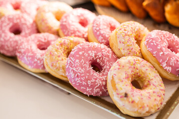 Colorful donuts with sprinkles on buffet table in hotel breakfast area, close-up. Sweet dessert, morning treat, and vibrant bakery presentation concept.