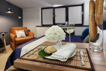 A well-arranged dining area features a beautiful flower centerpiece, fresh bread, and a glass of white wine in a stylish hotel room. Soft lighting creates a warm ambiance.