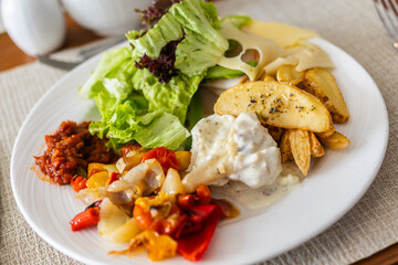 Plate with salad, roasted vegetables, potatoes, and cheese on dining table close-up. Healthy lunch option, balanced nutrition, and hotel meal concept.