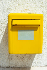 Yellow mailbox on bright white wall. Postal service, communication symbol, and street detail in sunny environment.