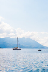 Sailboat anchored near mountainous coastline under soft sunlight. Coastal travel, maritime leisure, and scenic summer escape.
