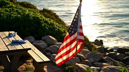 usa flag - A serene coastal scene featuring an American flag waving gently by a picnic table surrounded by lush greenery and rocks, with the ocean glistening in the background - Powered by Adobe