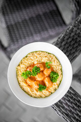 Creamy risotto with tomato sauce and parsley garnish served in a white bowl on a woven surface, presented in a top-down view with natural lighting for culinary emphasis