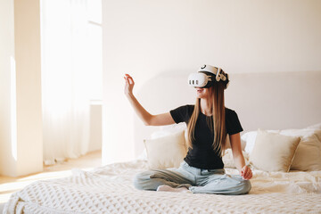 Young woman experiences virtual reality on a bed in a bright, spacious room during the daytime