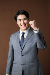 茶色背景でスーツを着たガッツポーズするビジネスマンの上半身　士業や不動産エグゼクティブのイメージ