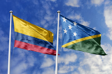 Waving flags of Colombia and Solomon Islands against a vibrant blue sky, symbolizing international relations and friendship.