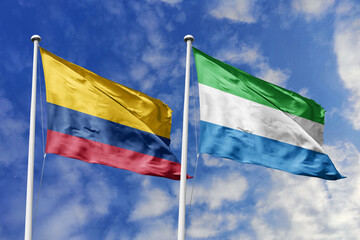 Waving flags of Colombia and Sierra Leone against a vibrant blue sky, symbolizing international...