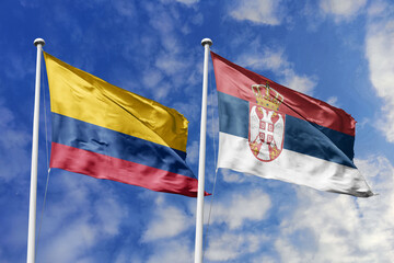 Waving flags of Colombia and Serbia against a vibrant blue sky, symbolizing international relations...