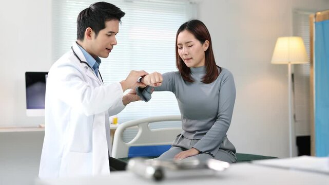 Doctor examines shoulder and arm of female patient in examination room at hospital.