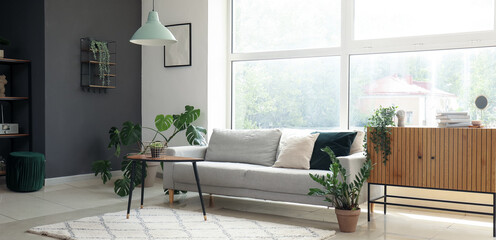 Interior of modern living room with cozy grey sofa near big window
