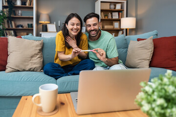 Surprised happy couple announcing their pregnancy to family and friends during a video call. Young future parents using laptop computer to share their good news and happiness.