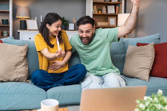 Surprised happy couple announcing their pregnancy to family and friends during a video call. Young future parents using laptop computer to share their good news and happiness. - Powered by Adobe