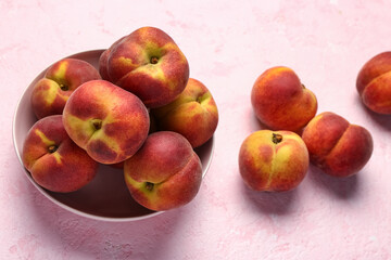 Bowl with sweet peaches on pink background