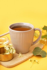 Cup of linden tea and bowl with honey on orange background
