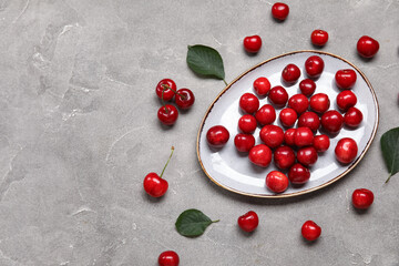 Plate with sweet cherries on grey background