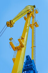 Bright yellow industrial crane structure rising against clear blue sky, showcasing engineering detail. Concept of crane technology, heavy machinery, urban port infrastructure