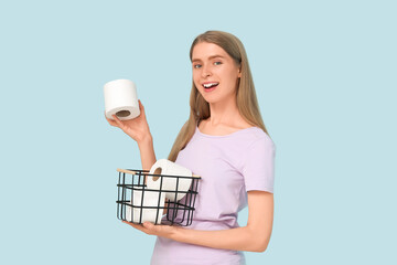 Young woman holding basket with toilet paper rolls on color background