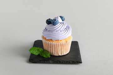 Board of tasty cupcake with blueberries on grey background