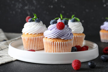 Plate of delicious cupcakes with blueberries, raspberries and mint on black background