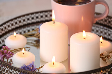 Tray with burning candles and flowers on table