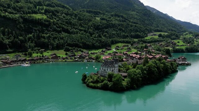 Aerial orbit arround castle Seeburg revealing the view of the turquoise lake Brienzersee Iseltwald surrounded by the alpmointains on a sunny summer day in Switzerland near Interlaken