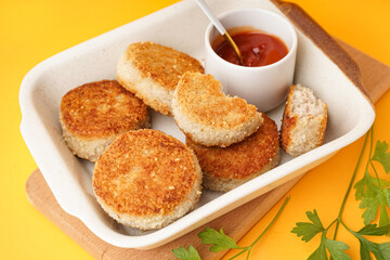 Baking dish of tasty meat cutlets on yellow background