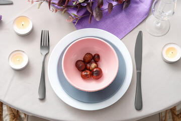 Autumn table setting with chestnuts and burning candles, closeup