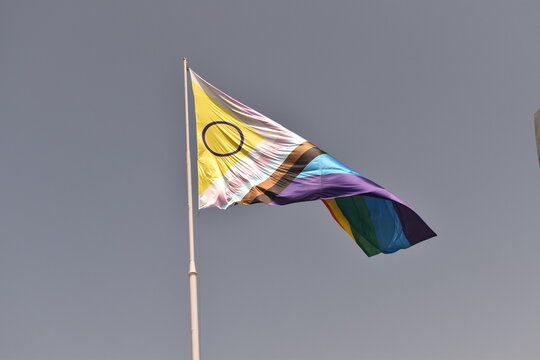 Intersex‑inclusive Progress Pride flag flying against a clear blue sky&mdash;symbolizing unity, visibility, and intersectional LGBTQIA+ pride