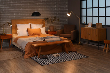 Interior of bedroom with armchair, glowing lamps and wooden bench at night
